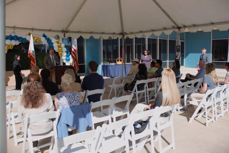 A seated crowd watching Board President John Boyd deliver remarks outside the Palm Springs Law Library.