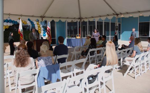 A seated crowd watching Board President John Boyd deliver remarks outside the Palm Springs Law Library.