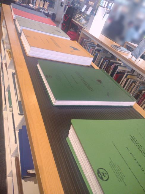 Six large atlases of Alaska's waters on top of a bookcase.