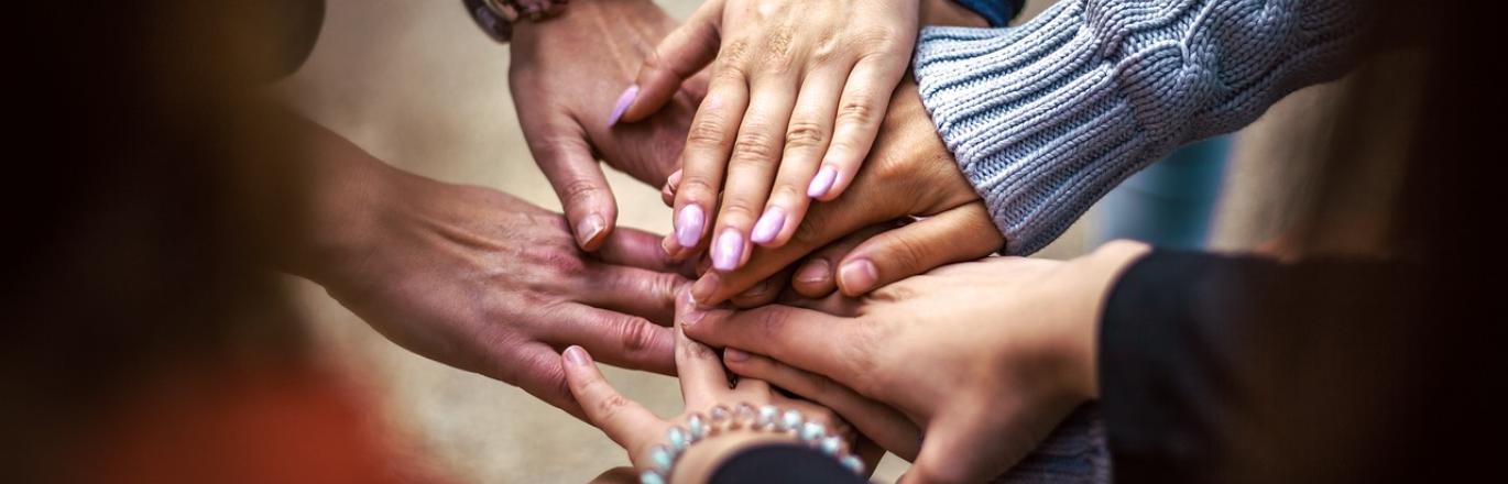 Photograph of hands overlapping in the center of a support circle.
