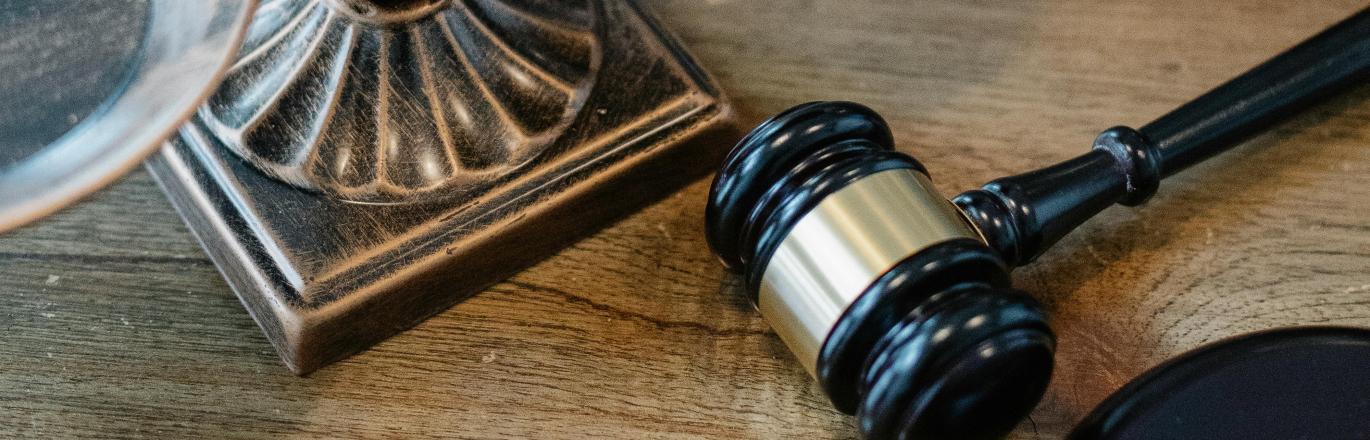 Metallic Scales of Justice atop a brown wooden table next to a gavel and set of binders