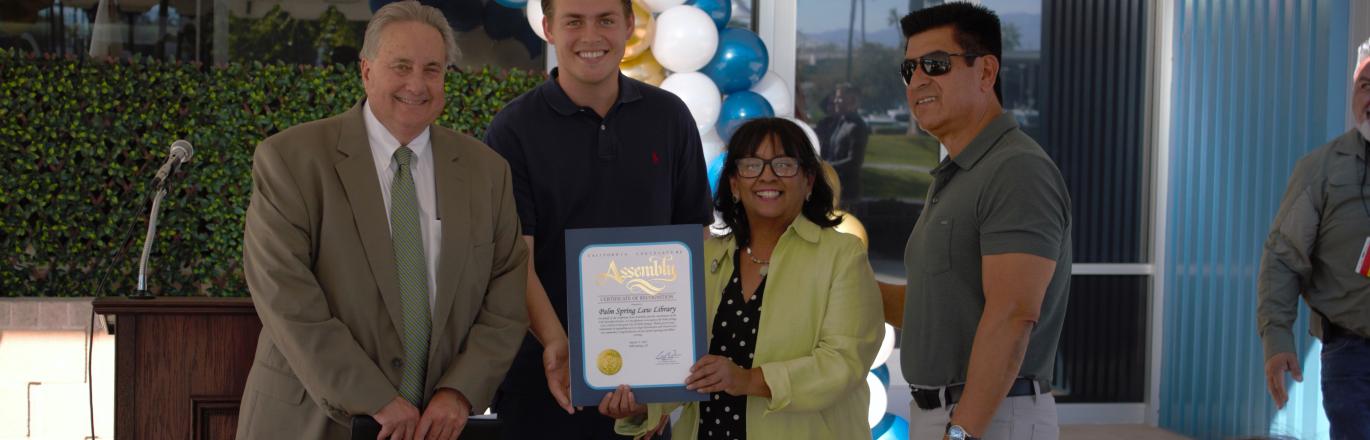Board President John Boyd, a representative of Assemblymember Greg Wallis, Deputy Chief of Staff Patricia Cooper, and County Facilities Management Director Vince Izaguirre posing with a certificate from the California State Assembly.