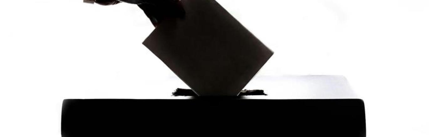 A silhouette of a hand placing a ballot into a ballot box.