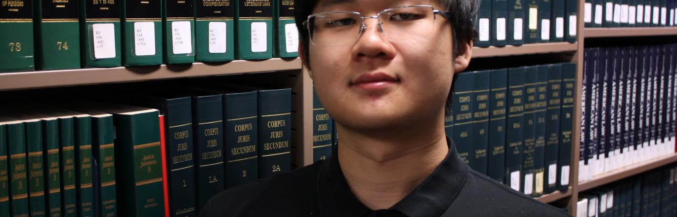 Photograph of Library Assistant Dean Se in front of a shelf of books.