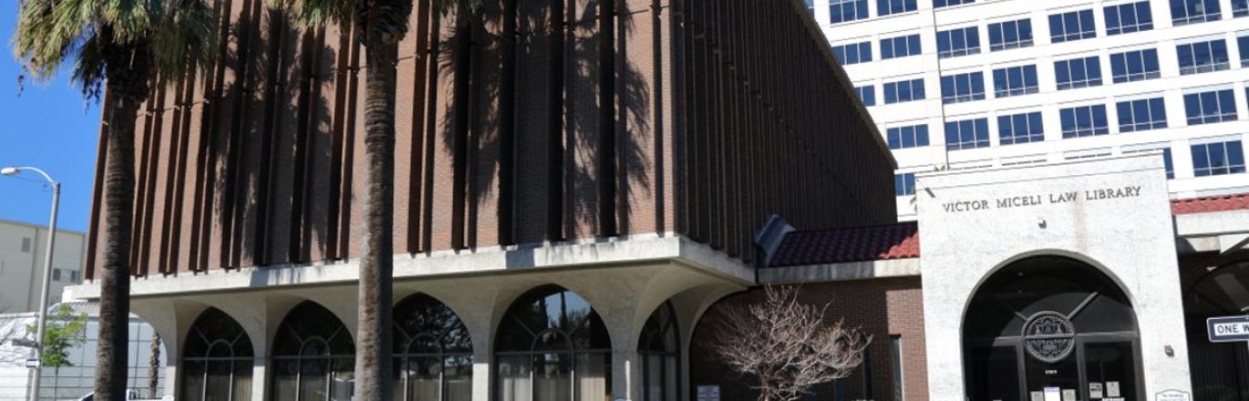 outside pic of the law library- a 3 story brown brick building with 2 palm trees out front