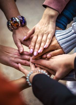 Photograph of hands overlapping in the center of a support circle.