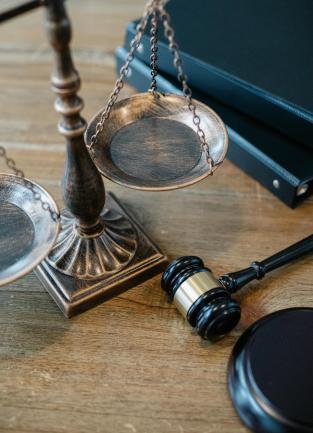 Metallic Scales of Justice atop a brown wooden table next to a gavel and set of binders