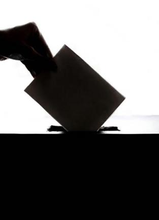 A silhouette of a hand placing a ballot into a ballot box.