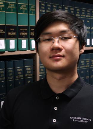 Photograph of Library Assistant Dean Se in front of a shelf of books.