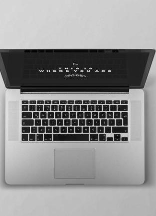 overhead view of a laptop with a green plant and black notebook to the left and a hand holding a cup to the right of the laptop