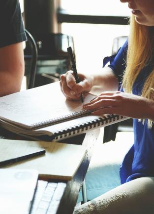 four people gather at a table with a laptop, notebook and coffee cup for a meeting